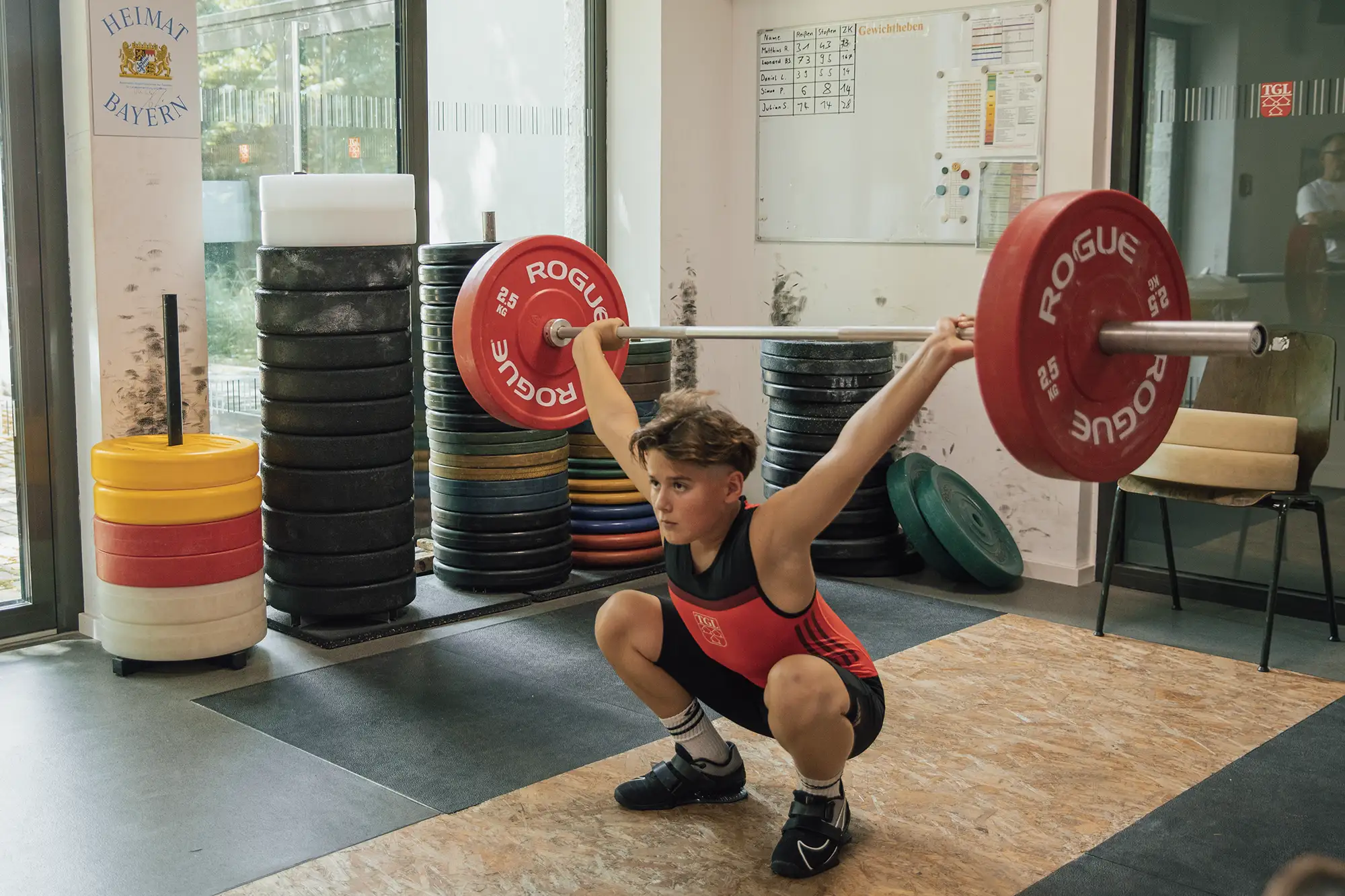Ein junger Gewichtheber der Turngemeinde Landshut hebt eine Langhantel in der Hocke im Sportverein.