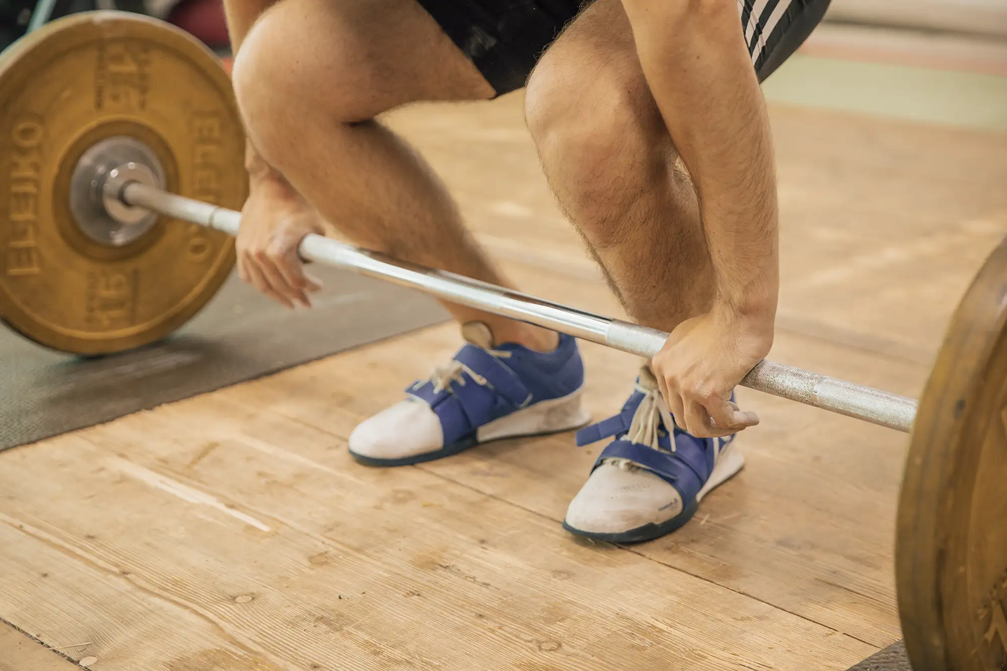 Ein Sportler hebt im Verein Turngemeinde Landshut eine schwere Langhantel auf einer Holzplattform.