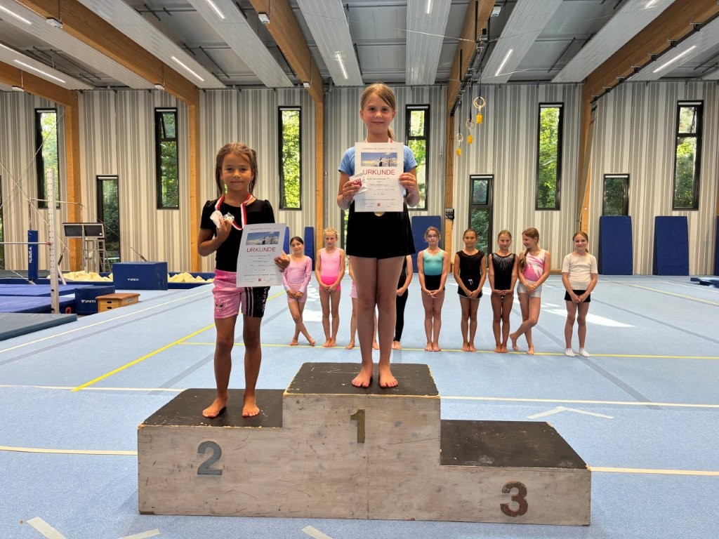 Zwei junge Mädchen stehen mit Urkunden auf dem Podest bei einem Turnwettbewerb der Turngemeinde Landshut im Verein.