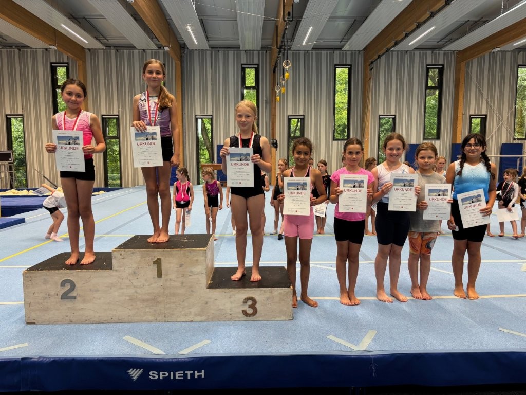 Junge Turnerinnen der Turngemeinde Landshut präsentieren stolz ihre Urkunden und Medaillen auf dem Siegerpodest.
