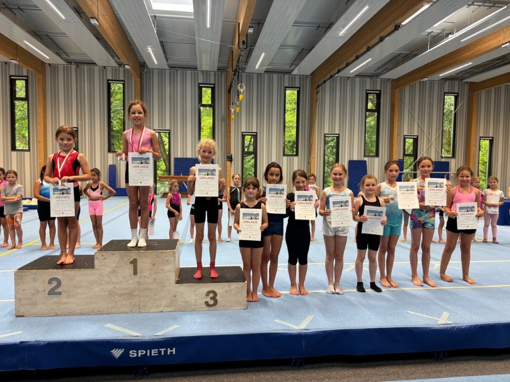 Junge Turnerinnen der Turngemeinde präsentieren stolz ihre Urkunden bei einer Sportveranstaltung in der Halle.
