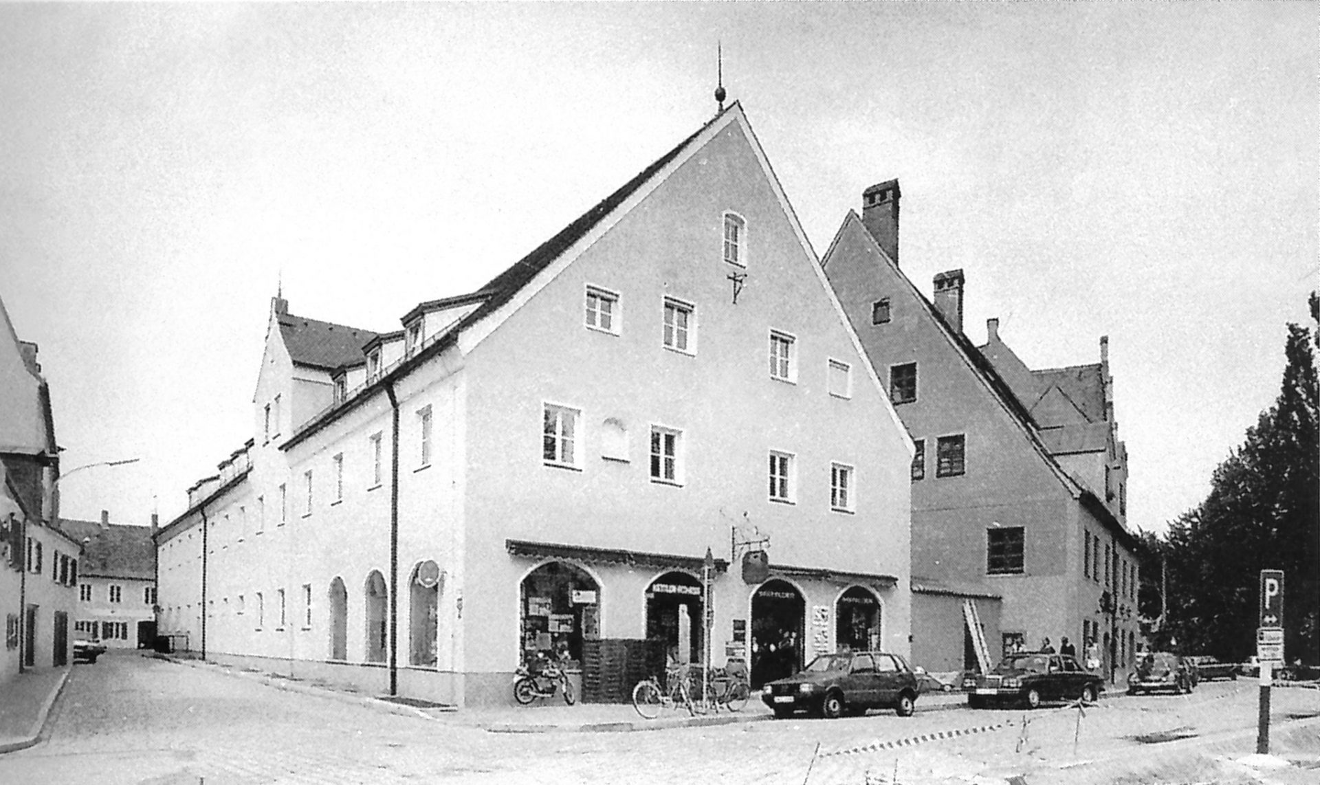 Ein historisches Gebäude in Landshut, das einst der Turngemeinde als Turnhalle diente, ist von Autos und Fahrrädern umgeben.